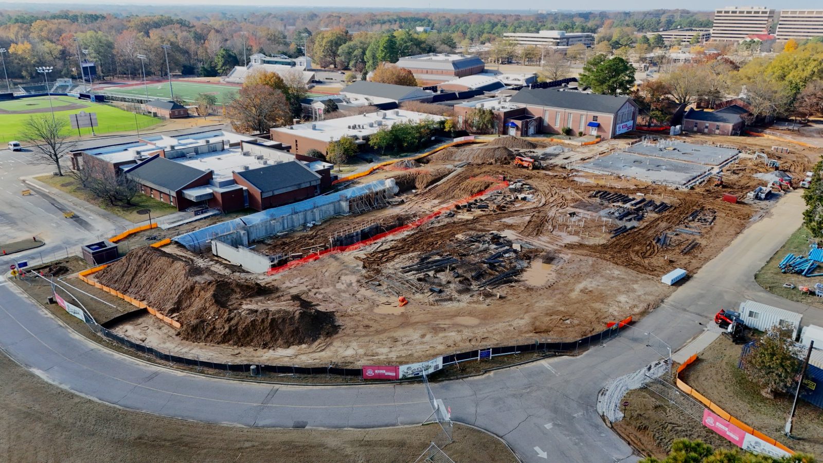Aerial construction progress photo of an East Memphis campus project showing poured foundations, rebar, a new retaining wall, and site grading