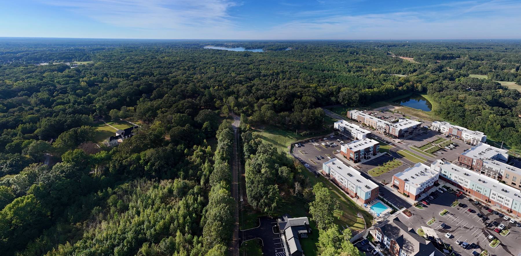 Aerial view of wooded land beside a new mixed-use development in Lakeland, Tennessee, with a lake on the horizon